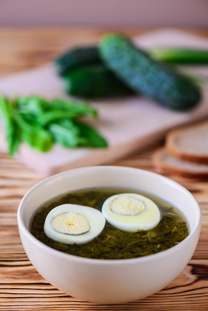 Sauerampfer-Suppe mit gekochten Eiern auf einem Holztisch.