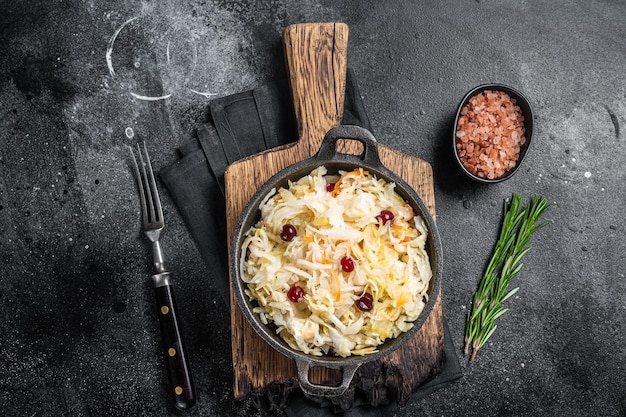 Sauerkraut in einer Pfanne mit schwarzem Pfeffer und Cranberry Fermentierter Kohl Schwarzer Hintergrund Ansicht von oben