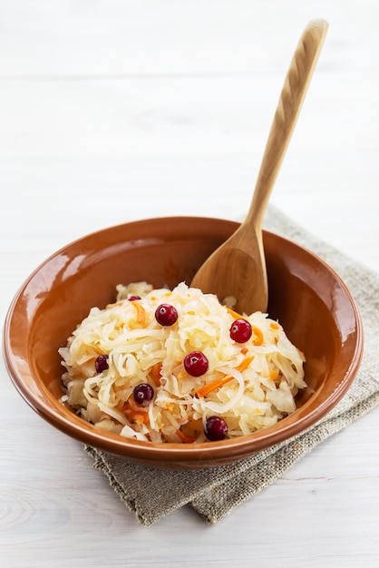 Sauerkraut mit Preiselbeeren in einer Tonschale mit einem Holzlöffel auf einer Serviette