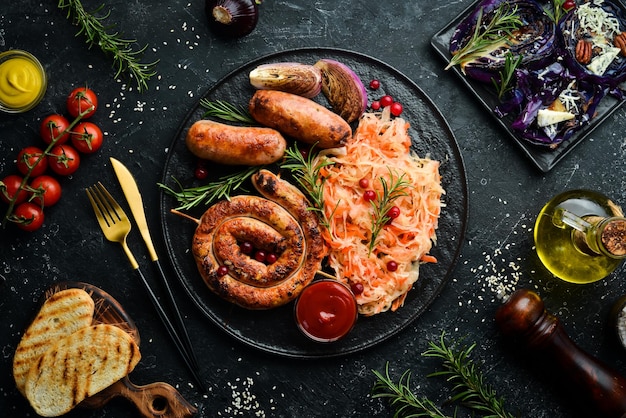 Sauerkraut und gegrillte Würstchen mit Rosmarin und Preiselbeeren auf einem schwarzen Teller Traditionelles deutsches Gericht Draufsicht auf schwarzem Steinhintergrund