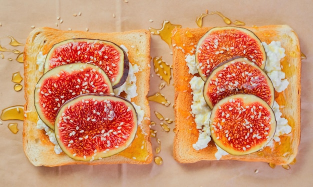 Sauerteig-Weizen-Toast mit Ricotta-Käse, frische Feigen mit Honig und Sesamsamen, Layout auf Kraftpapierunterlage Draufsicht auf Toast mit Feigen, Frühstücksidee mit saisonalen Früchten