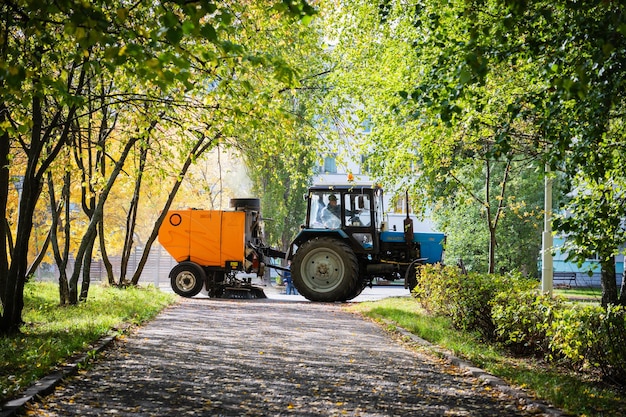 Saugkehrmaschine, die von einer Traktorarbeit im Herbstpark gezogen wird.