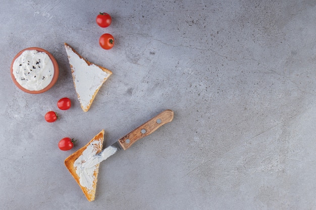 Saure Sahne, Kirschtomaten und Toastbrot auf Steintisch.