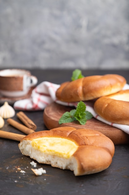 Saures Sahnebrötchen mit Tasse Kaffee auf schwarzem Betonhintergrund und Leinentextil. Seitenansicht, Kopierraum.