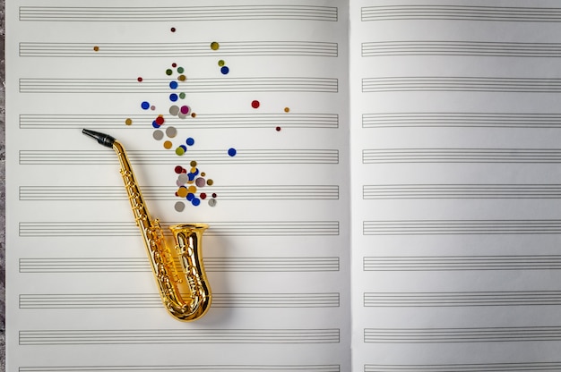 Saxofón dorado con lentejuelas de colores sobre fondo de cuaderno de música