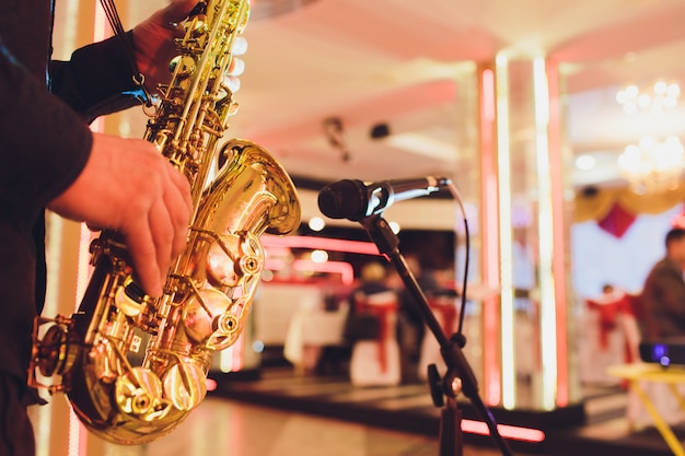 Saxofón dorado en manos de un músico cerca del micrófono.