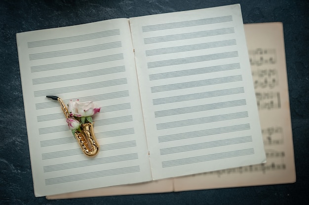 Saxofone dourado com rosa no fundo do caderno musical com as notas