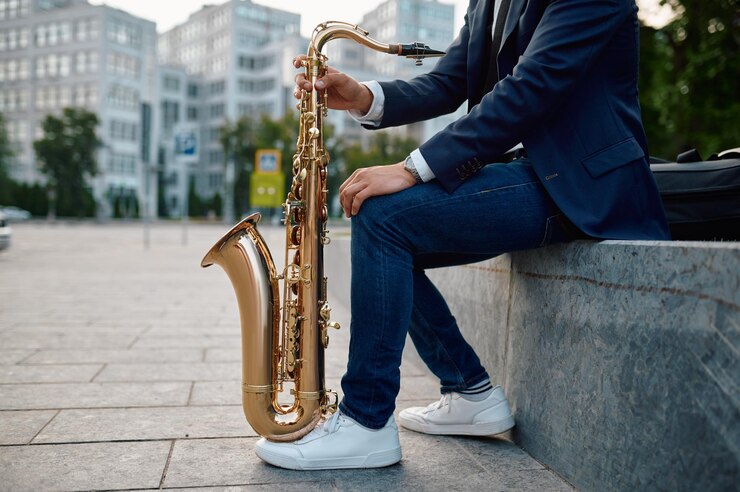 Foto saxofonista masculino posa con saxofón, edificios en el fondo, talento joven. músico con saxo al aire libre, actuación musical en la ciudad. intérprete de jazz, música urbana