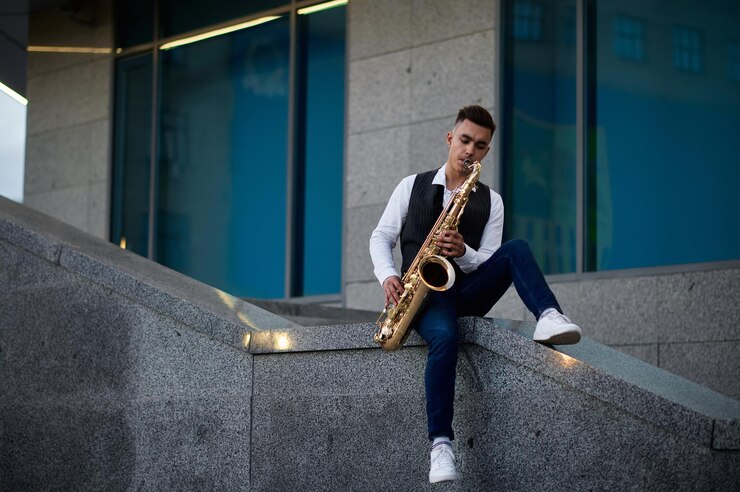 Foto saxofonista masculino con saxofón dorado posa en las escaleras de la calle, talento joven. músico con saxo al aire libre, actuación musical en la naturaleza. intérprete de jazz, estilo urbano