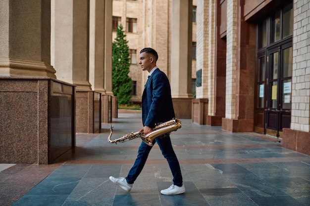 Saxofonista masculino tiene instrumento en la calle, talento joven. Músico con saxo al aire libre, actuación musical en la ciudad, intérprete de jazz