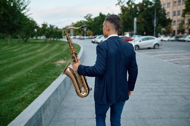 El saxofonista toca la melodía en el banco en el parque de la ciudad