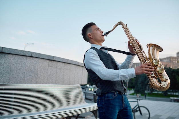 El saxofonista toca la melodía en el banco en el parque de la ciudad