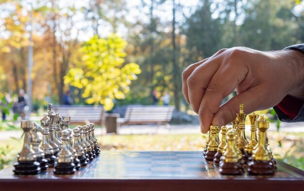 Schachspiel im Freien. Schachbrett mit Figuren, Nahaufnahme, Hand macht den ersten Zug. Selektiver Fokus.