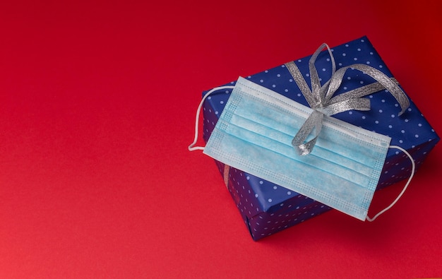 Schachtel mit Geschenk in blauem Papier mit Tupfen mit silberner Schleife mit medizinischer Schutzmaske