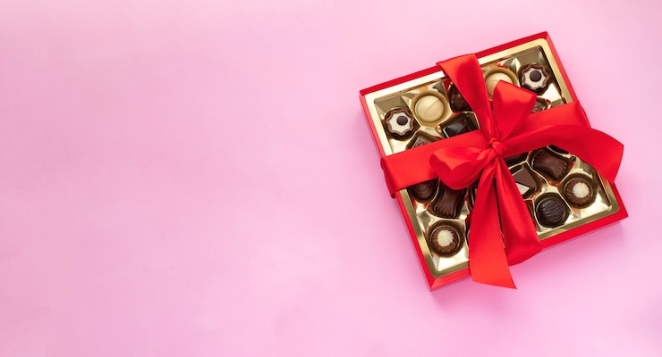 Foto schachtel schokoladenpralinen mit roter schleife auf rosa