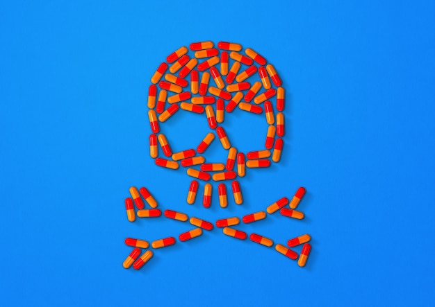 Schädel aus orangefarbenen Kapselpillen auf blauer Oberfläche. 3D-Illustration
