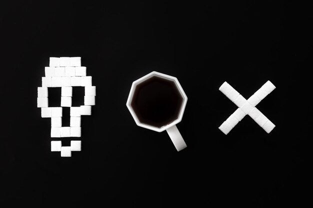 Schädelknochen aus Zucker und Tasse Kaffee auf schwarzem Hintergrund flach gelegt