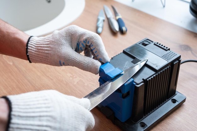 Schärfen eines Messers auf einem elektrischen Schärfer zu Hause Die Hand des Mannes treibt die Messerklinge zwischen den blauen Schärfern Staubfliegen auf der Maschine