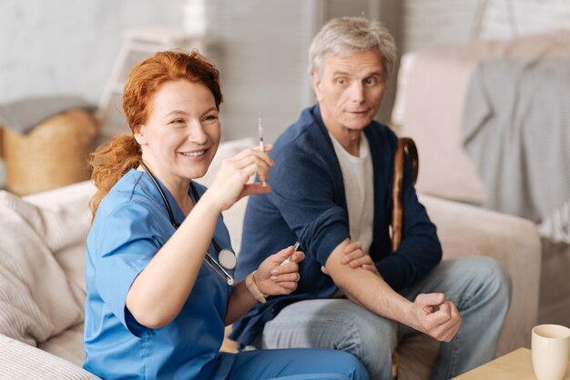 Schätzung der Dosierung. Ordentlich entschlossen erfahrene Therapeutin, die ihrer Patientin eine Dosis Vitamine zur Stärkung ihres Immunsystems gibt, während sie ihn zu Hause besucht