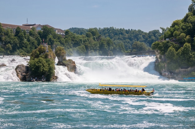 Schaffhausen, suíça - 20 de junho de 2017: ver as cataratas do reno é a maior cachoeira da europa e as pessoas em um barco ao redor dela. dia de verão com céu azul