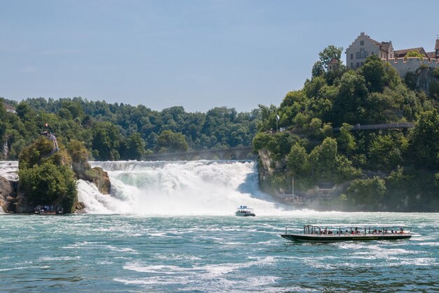 Schaffhausen, Suiza - 22 de junio de 2017: Barco con gente flotando a la cascada de las cataratas del Rin. Es uno de los principales atractivos turísticos. Día de verano con cielo azul