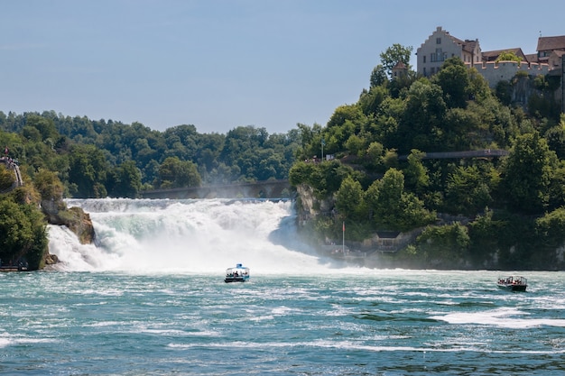 Schaffhausen, Suiza - 22 de junio de 2017: Barco con gente flotando a la cascada de las cataratas del Rin. Es uno de los principales atractivos turísticos. Día de verano con cielo azul