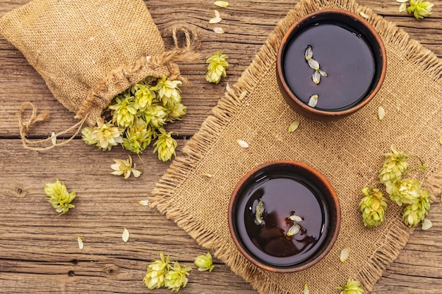 Schale beruhigender Kräutertee mit frischen wilden Hopfen. Hopfenzapfen im Sack auf Weinlesebrettern