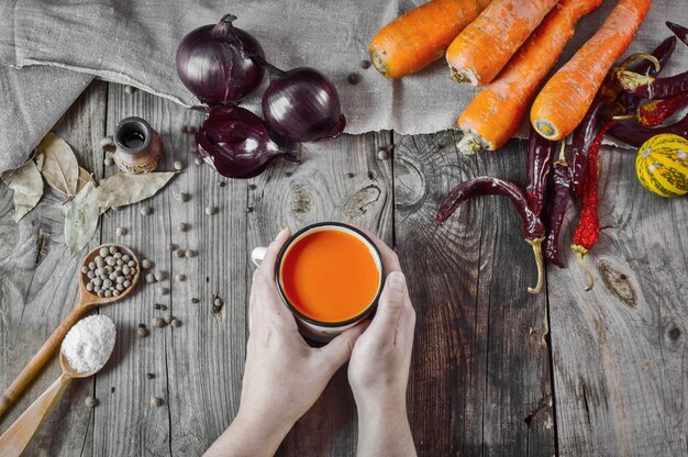 Schale Karottensaft in den weiblichen Händen auf einer grauen Holzoberfläche