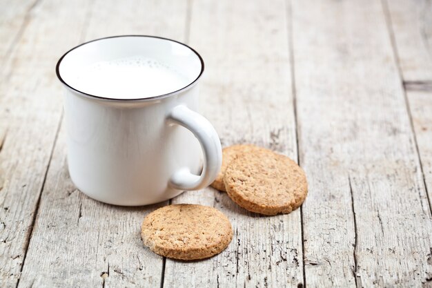 Schale Milch und einige frische gebackene Haferplätzchen auf rustikalem Holztisch