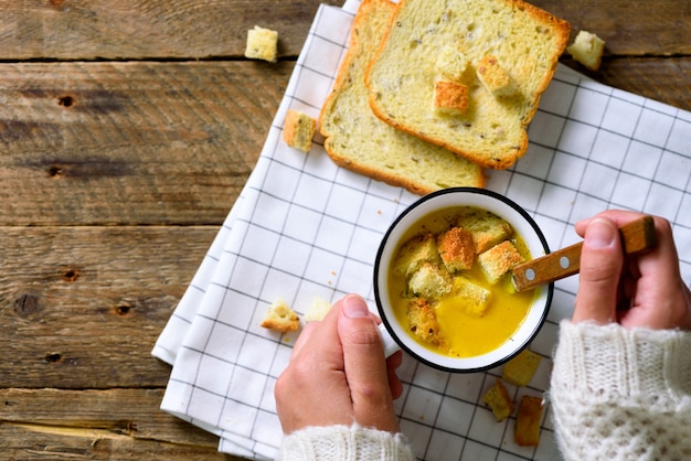 Schale mit Karottencremesuppe in den Mädchenhänden auf hölzernem rustikalem