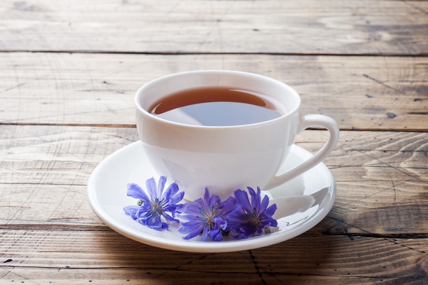 Schale mit Zichoriengetränk und blauen Zichorienblumen auf Holztisch