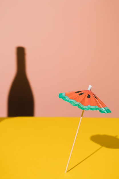 Scharfer Schatten der Champagnerflasche und ein Cocktailregenschirm auf gelbem und rosa Hintergrund. Kreatives Konzept der Geburtstagsfeier. Minimale abstrakte bunte lebendige Tapetenidee. Sommergetränke.