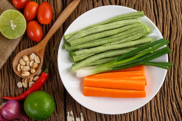 Scharfes Essen im thailändischen Stil Som Tum Essen Konzept Requisiten Dekoration Knoblauch Zitrone Tomaten Chili langgeschlüpfte Bohnen Frühlingszwiebeln Schalotten und Karotten und Erdnüsse auf Holz Löffel auf Holz Tisch