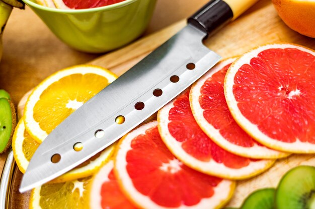 Scharfes Küchenmesser auf Schneidebrett neben geschnittener Grapefruit und anderen Früchten