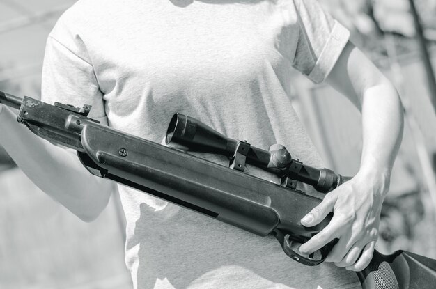 Scharfschützengewehr in weiblichen Händen Frau hält ein Gewehr mit einem optischen Visier in Nahaufnahme