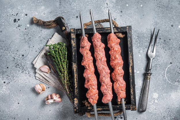 Schaschlik aus rohem Lamm- und Rinderhackfleisch, türkischer Adana-Kebab. Grauer Hintergrund. Ansicht von oben.