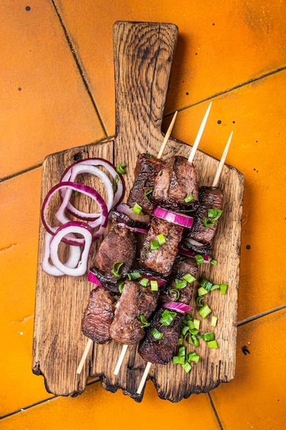 Schaschlik mit Rind- und Lammfleischzwiebeln und Kräutern auf Spießen Orangefarbener Hintergrund Ansicht von oben