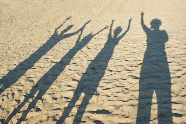 Schatten auf dem Sand von den erhobenen Händen der Eltern der Familie und der Kinder