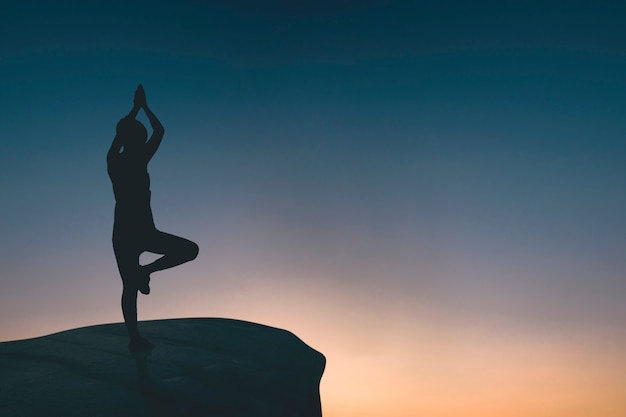 Schattenbild der Frau Yoga auf Felsen tuend