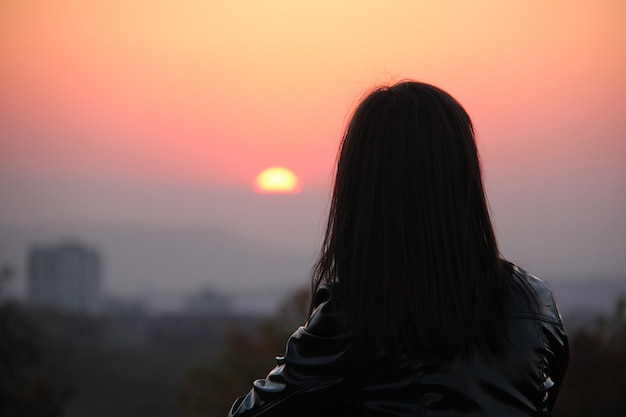 Schattenbild der jungen Frau im roten Sonnenuntergangslicht, das weit weg schaut.