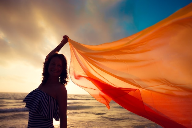 Schattenbild der jungen Frau mit Seidenstoff am Strand