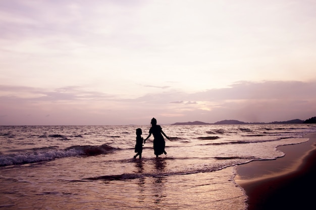 Schattenbild der Kinder, die am Strand bei Sonnenuntergang spielen