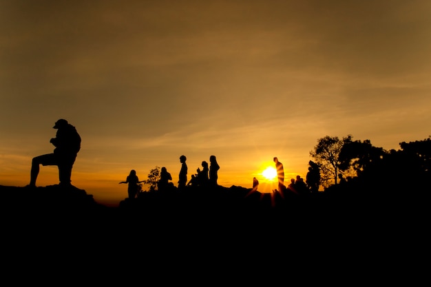 Schattenbild der Leute entspannen sich an der Klippe und den Bergen mit Sonnenuntergang am Abend