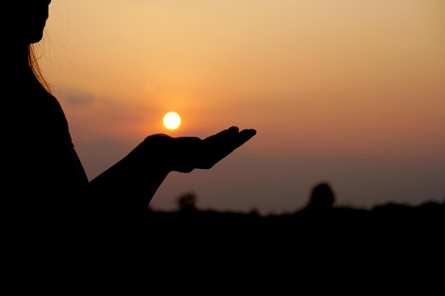 Schattenbild der menschlichen Hand, die angehoben wird, um einen Wunschsonnenunterganghintergrund zu machen