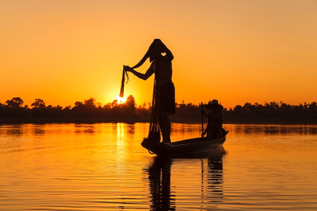 Schattenbild des Fischers mit Netz auf dem See bei Sonnenuntergang