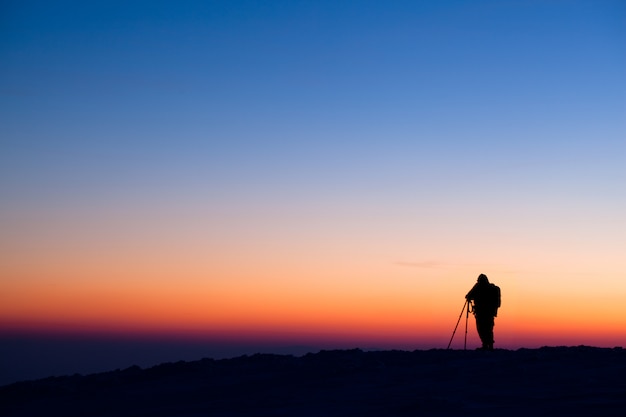 Schattenbild des Fotografen, der auf Hügel steht und Foto des Abendtals macht