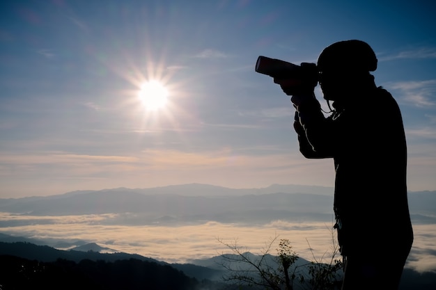 Schattenbild des freien und glücklichen Fotografen mit Kamera zur Sonnenuntergangzeit