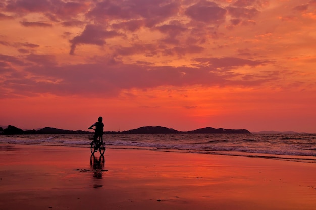 Schattenbild des Jungen Fahrrad auf dem Strand mit drametic Himmel fahrend