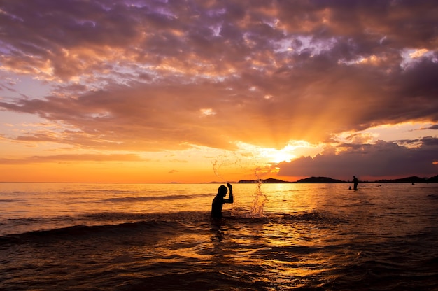 Schattenbild des Jungen spielend im Meer bei Sonnenuntergang