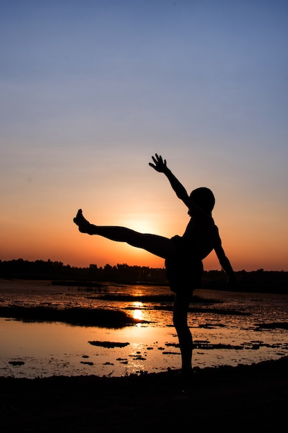 Schattenbild des Jungen stehen und mit dem Sonnenuntergang spielen.